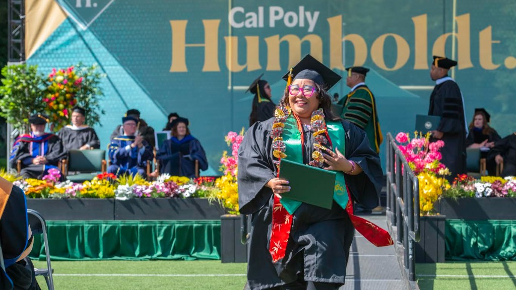 A female student in graduation regalia walking on the ceremony field.
