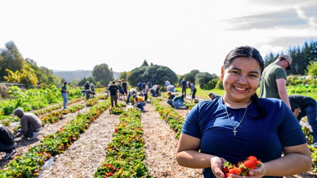 A female student smiling while holding produce and standing in a farm area.