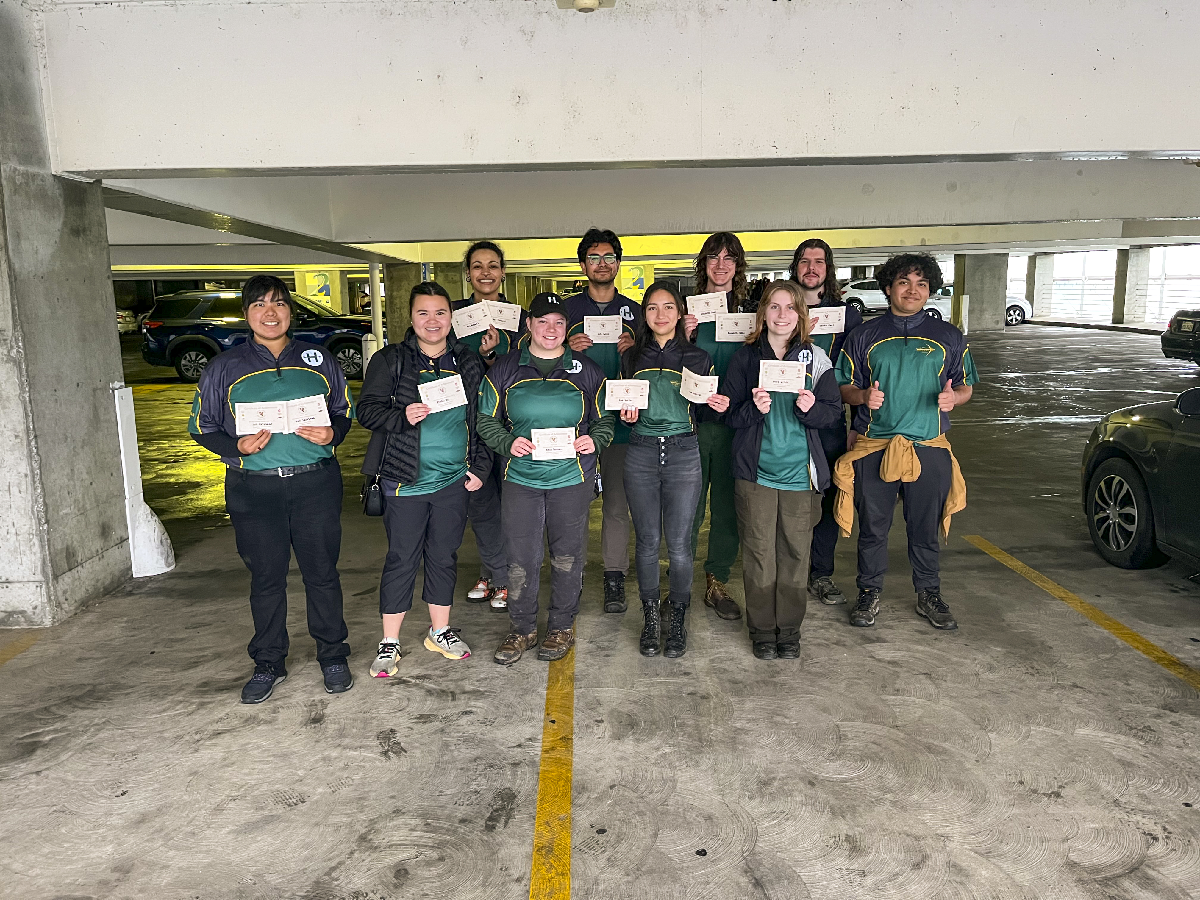 A group of archery students standing in a parking garage holding certificates. 