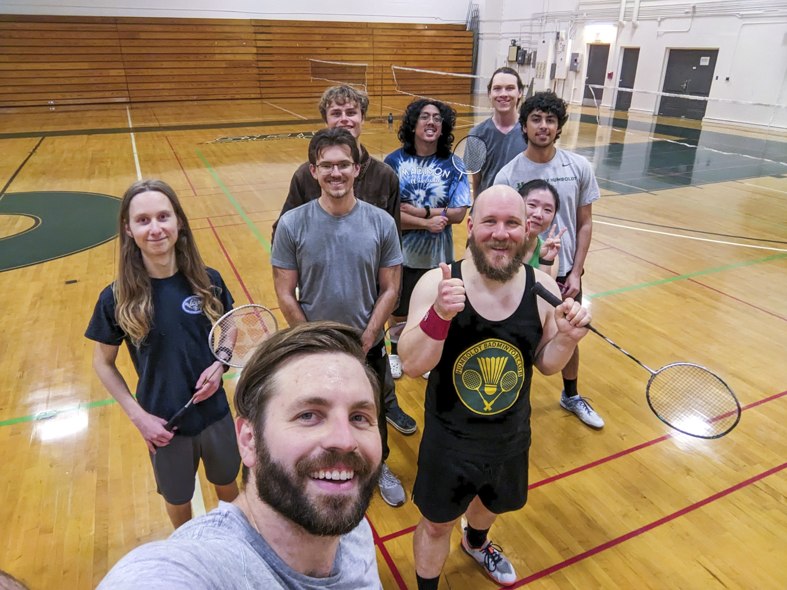 A selfie of nine badminton club members on the court with their rackets.