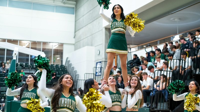 The cheer team at a basketball game lifting a member up in a stunt.