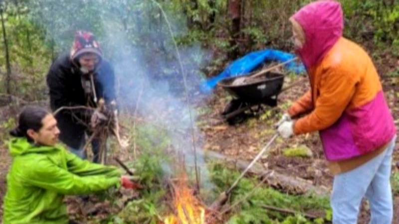 Three students in bright jackets outside in the forest making a fire. 