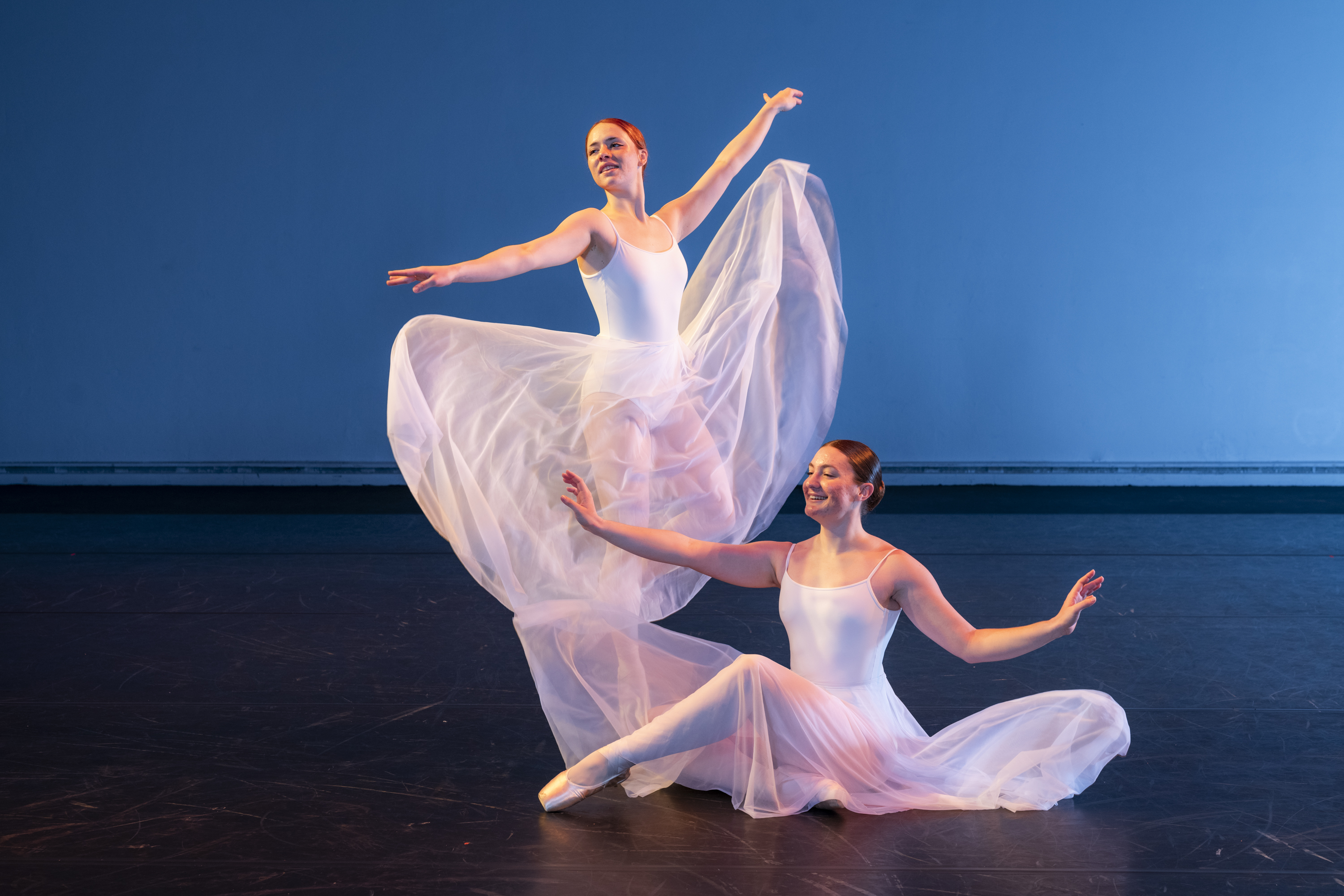 Two dance performers posing on the floor and standing in flowey costumes.