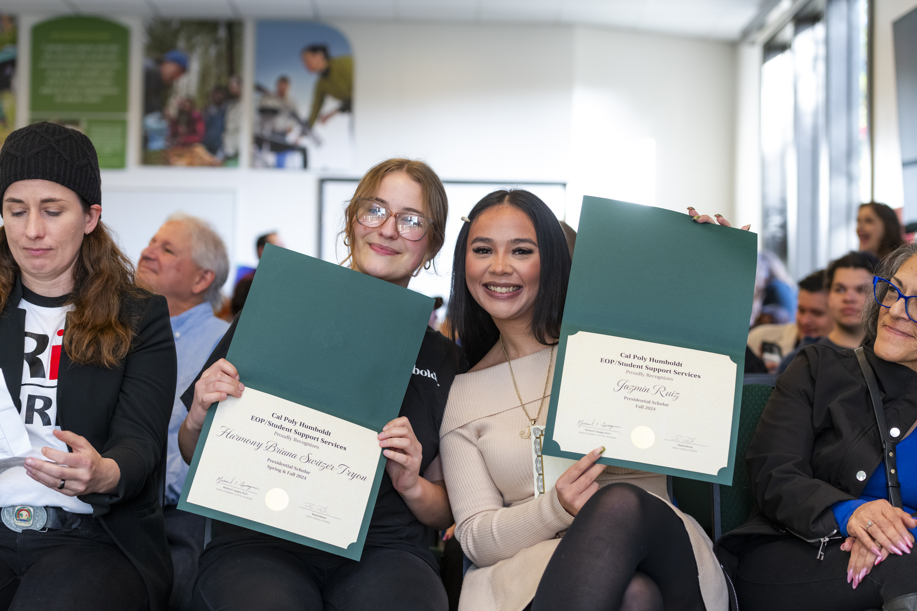Two EOP students smiling and holding up recognition certificates in a crowd.
