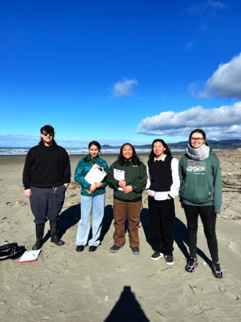 Five students standing and smiling at the beach.