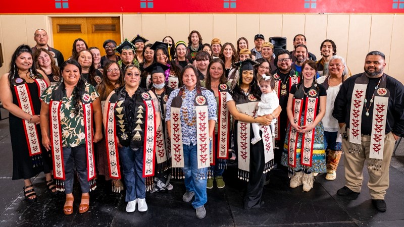 A large group of native graduates in their graduation regalia and sashes.