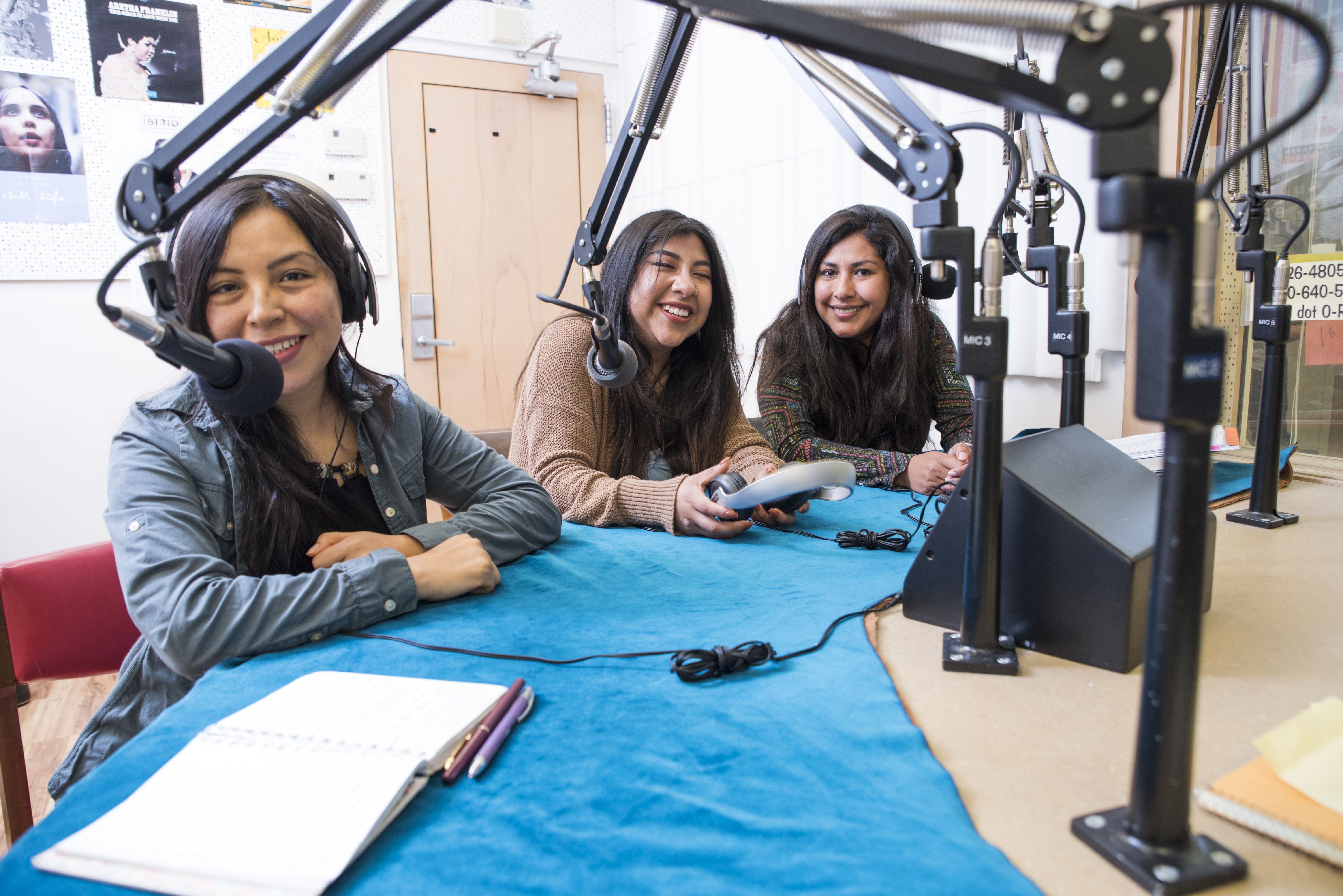 Three female students smiling in front of microphones in a recording studio.