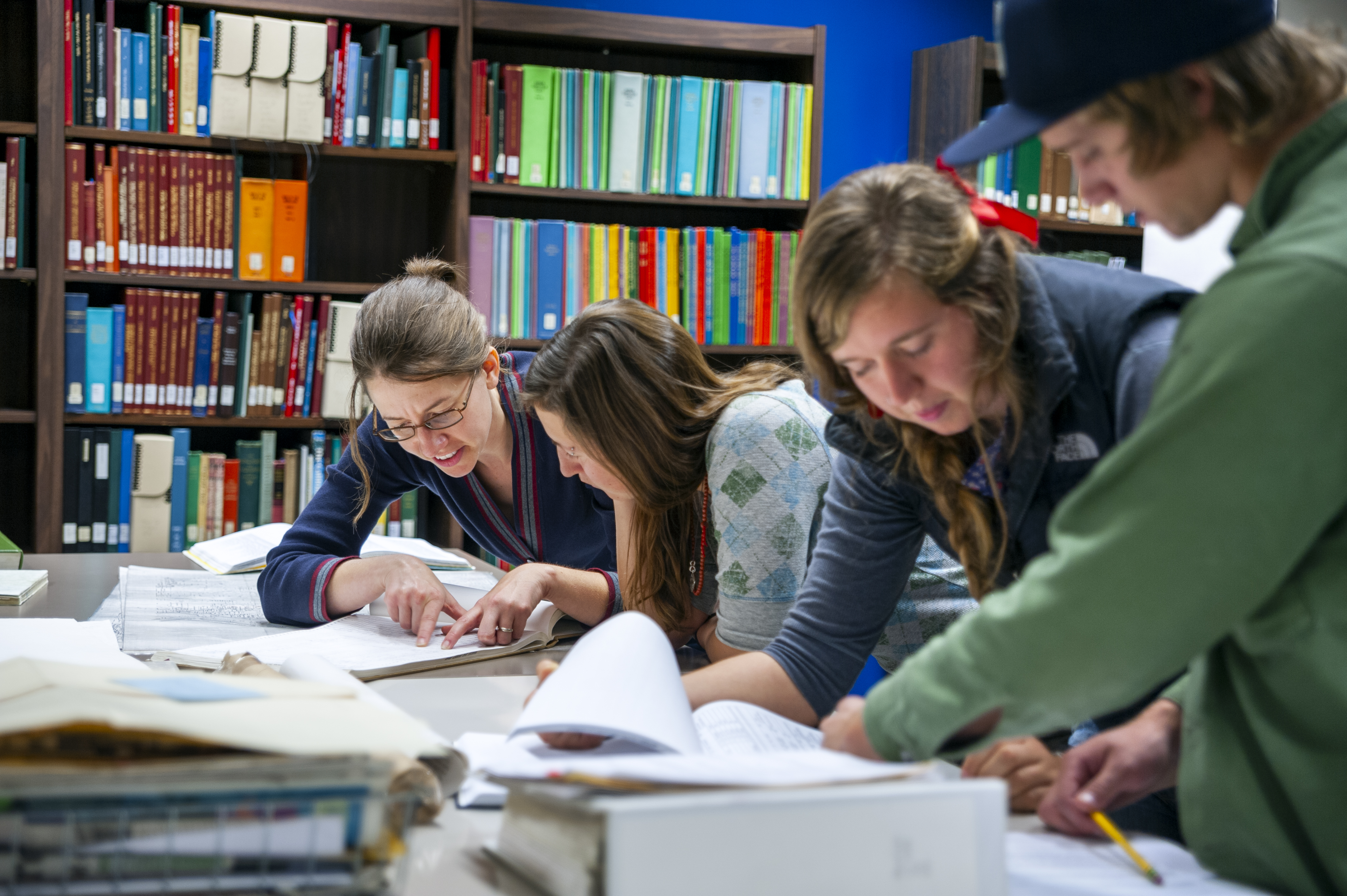 Four students reviewing manuscripts at a table in the library.