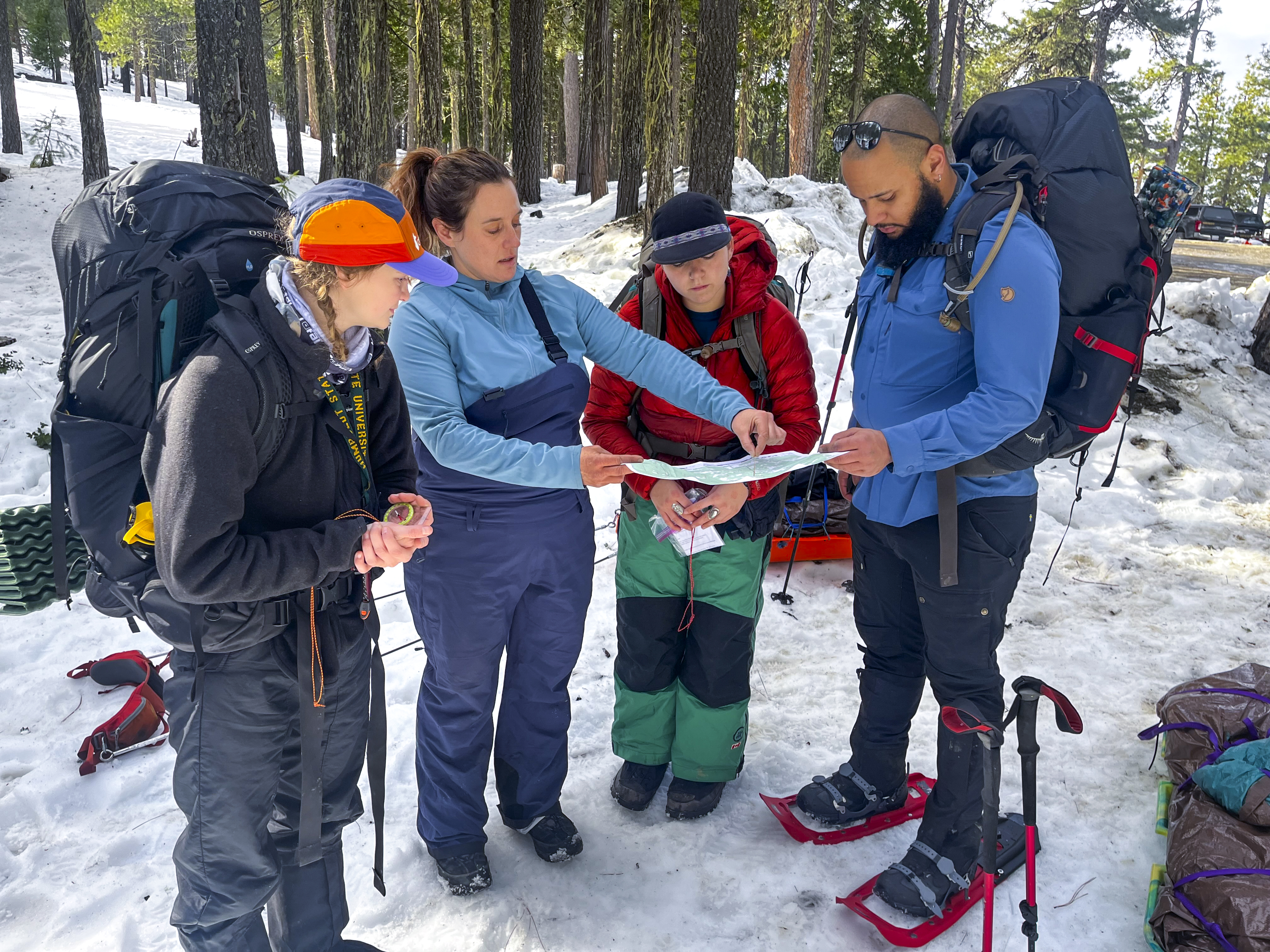 Four recreation students and faculty reviewing a map outside in the snow.