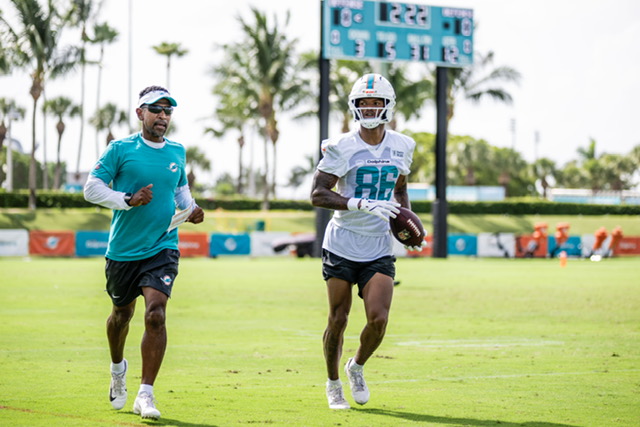 A photo of Robert Prince (left) training and coaching a team member of the NFL's Miami Dolphins on a practice field. 