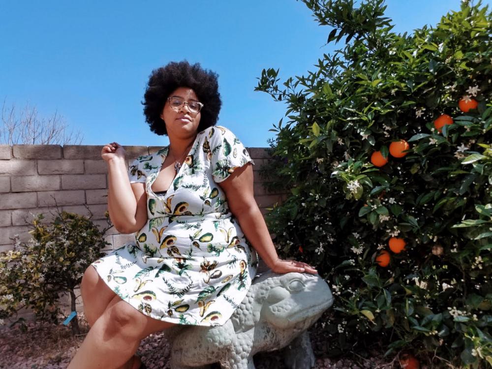 Sabina Gallier sitting next to a citrus tree wearing a dress. 