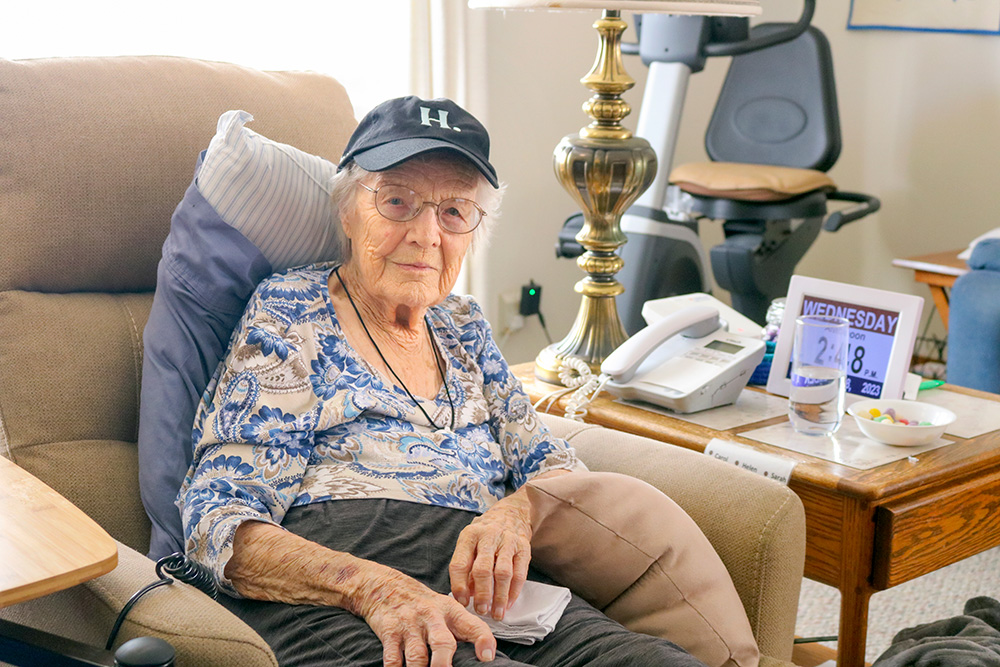 A photo of 102-year-old alum Sarah Franklin sitting on a chair wearing a Humboldt "H dot" baseball cap. 