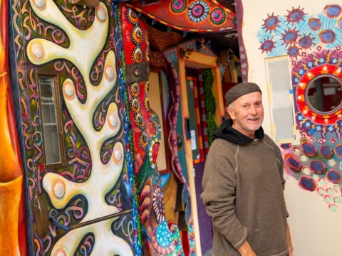 A photo of artist David White posing in front of the art hallway he created.