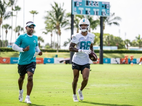 A photo of Robert Prince (left) training and coaching a team member of the NFL's Miami Dolphins on a practice field. 