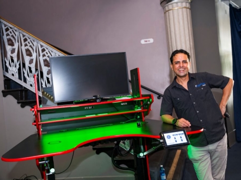A photo of Vico Hernandez standing next to his innovative ErgoFlex Desk at regional commencement.