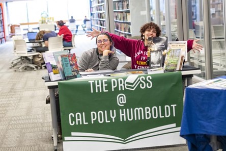 Two students sitting behind a table advertising The Press.