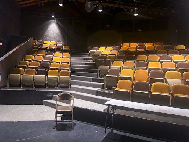 A stage view of Gist Hall theater with mis matched colored seats.