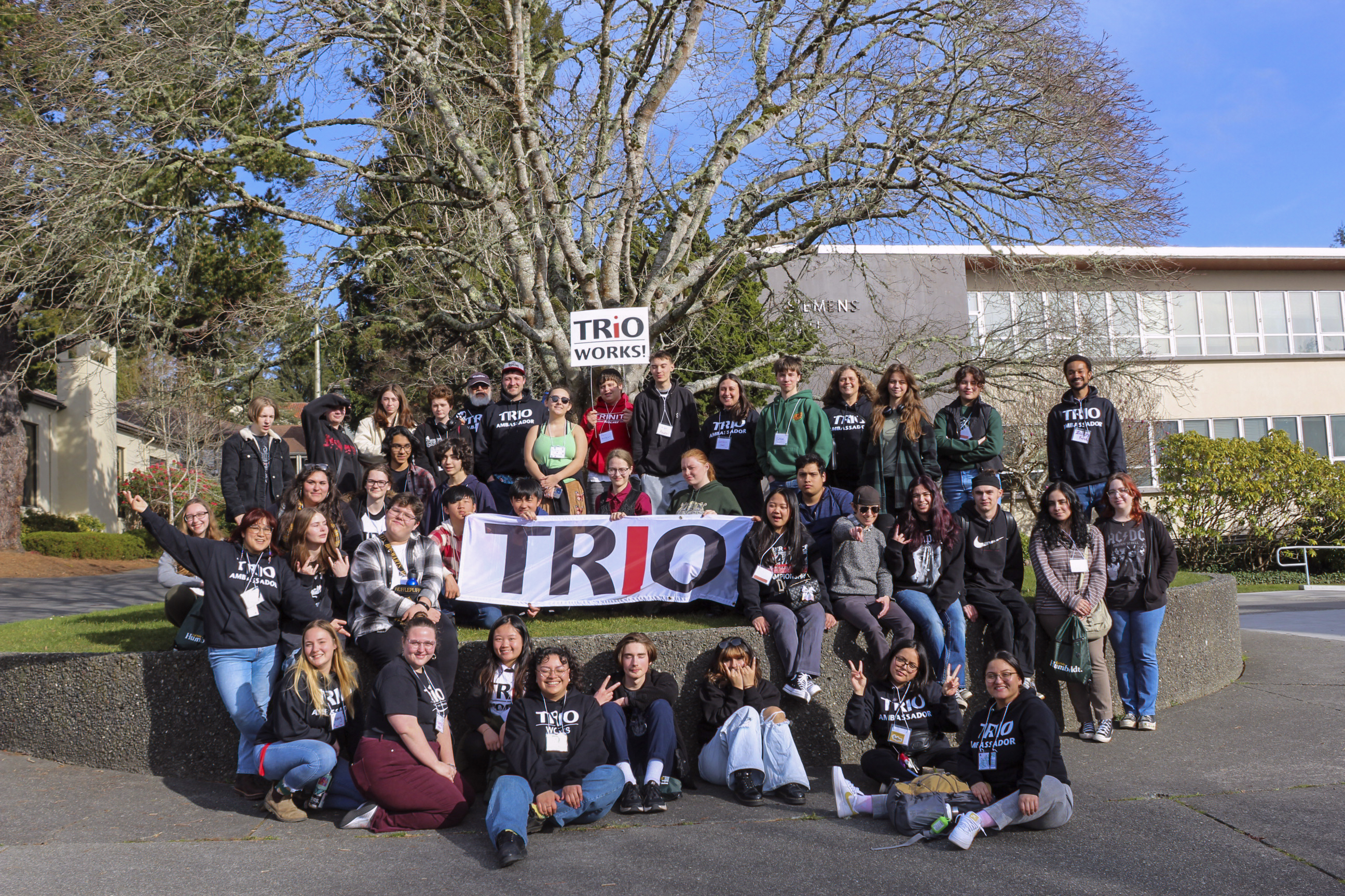 A large group of TRIO students with a banner in front of the tree at Library Circle.