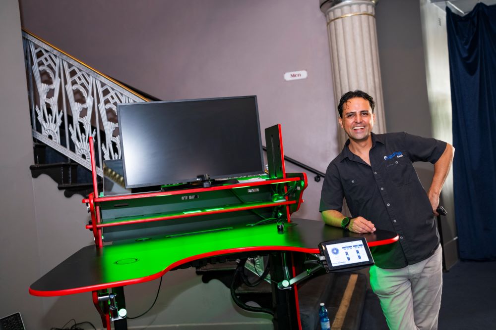 A photo of Vico Hernandez standing next to his innovative ErgoFlex Desk at regional commencement.