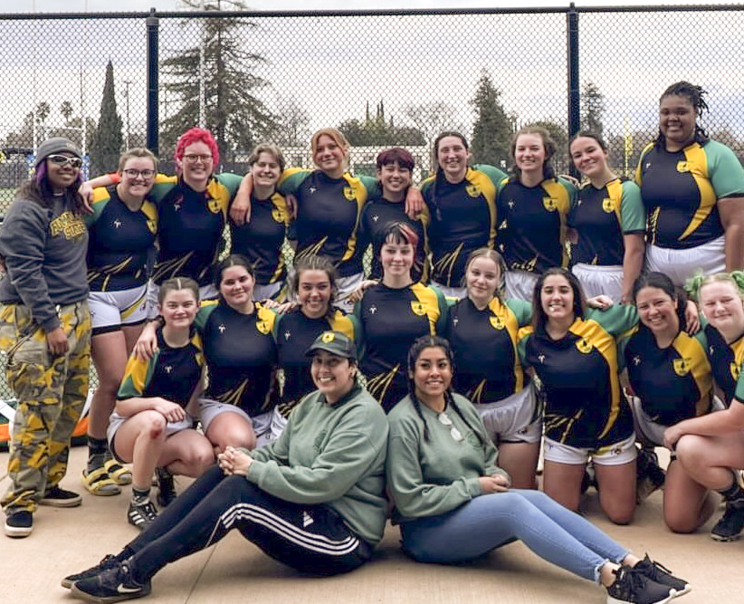 Team photo of women's rugby team in uniform in front of a field.
