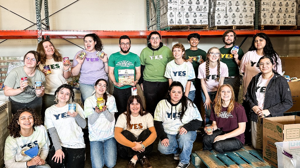 A group of 17 student volunteers in two rows showcasing canned food.